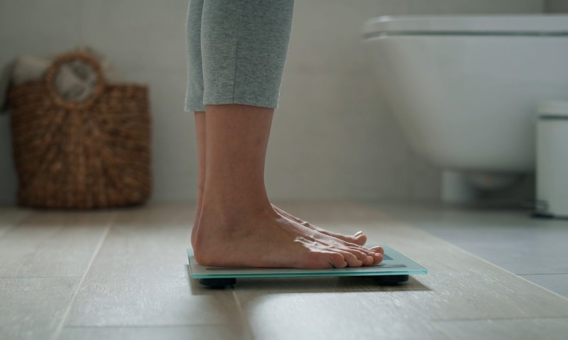 Osoba stoji na vagi, meri svoju telesnu težinu