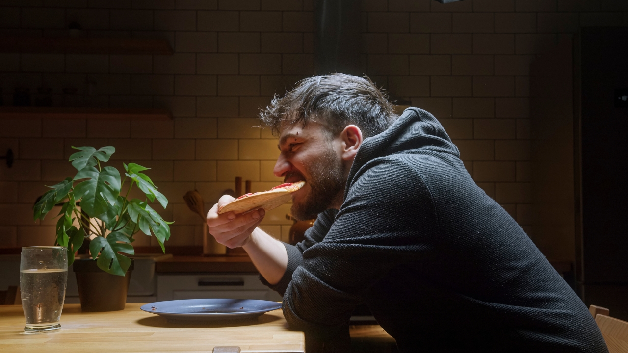 Muškarac noću u kuhinji jede picu i pokazuje pojačan apetit usled manjka sna